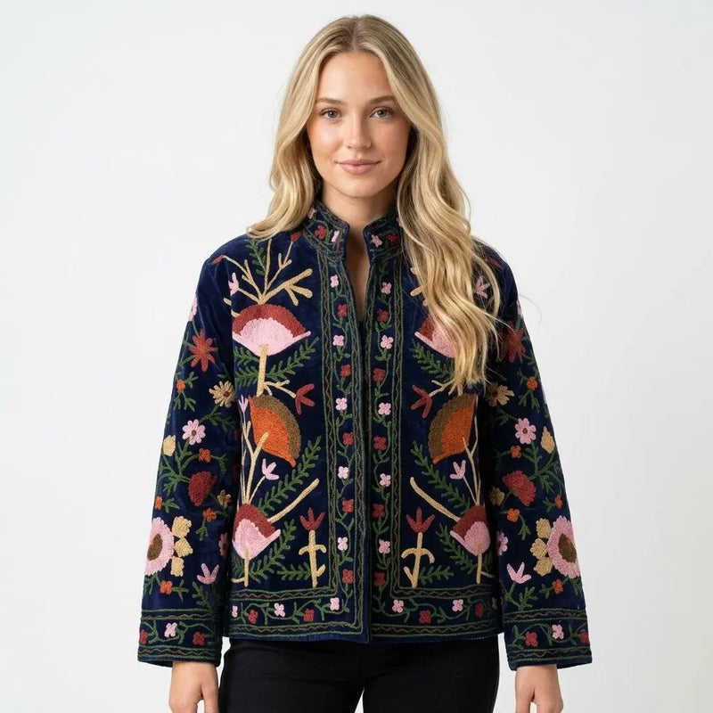 Woman wearing a dark blue embroidered jacket with colorful floral and bird patterns on a white background